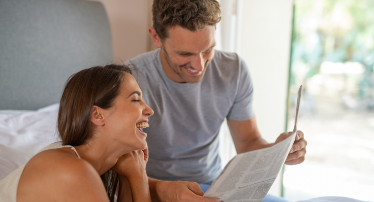 Un homme et une femme lisent ensemble un magazine en riant. 
